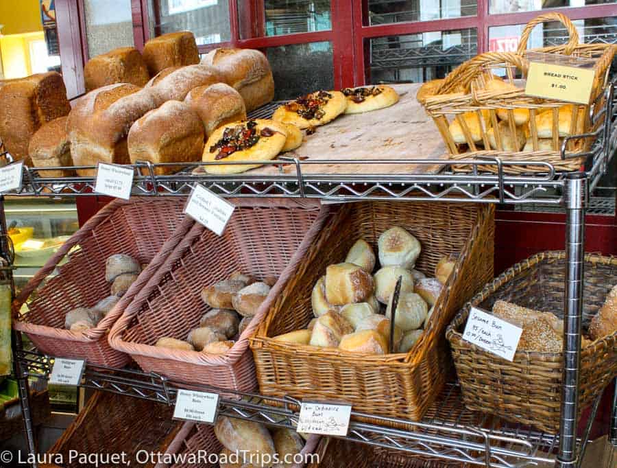 wicker baskets filled with different kinds of bread and buns on a wire rack at pan chancho bakery in kingston, ontario.
