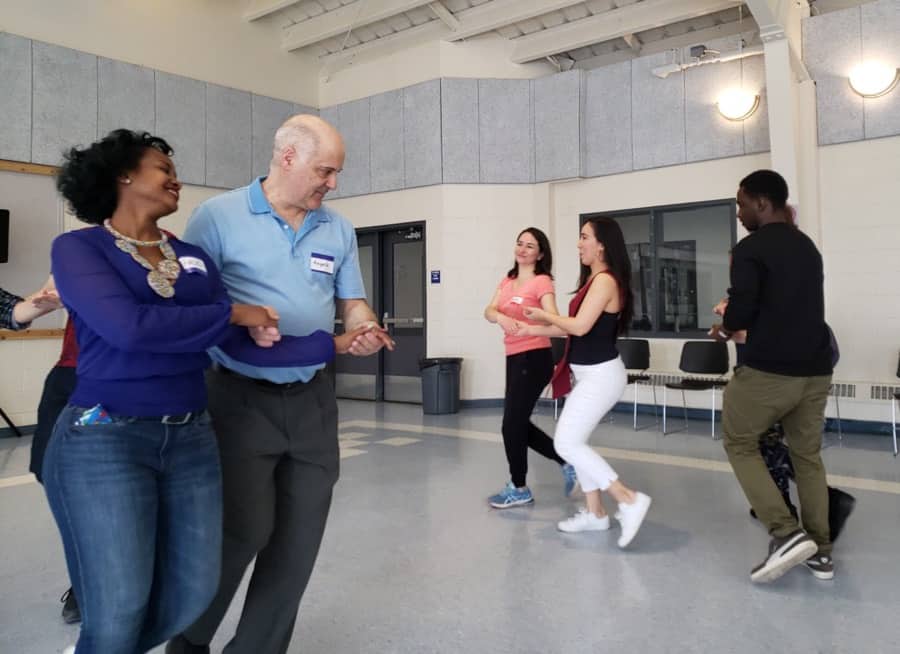 four couples dancing with linked arms in a modern gym