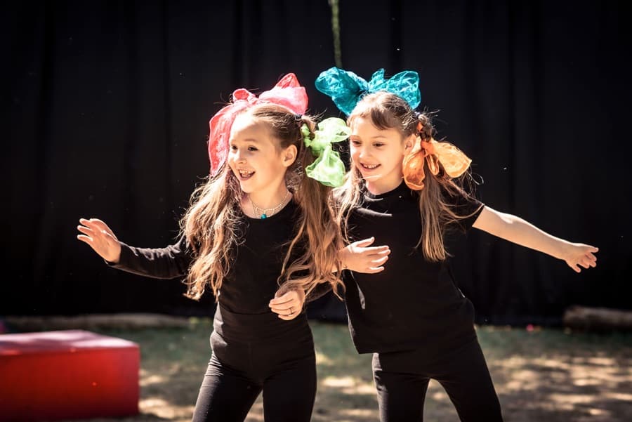 Two smiling young girls in black clothing, with big bows in their hair.