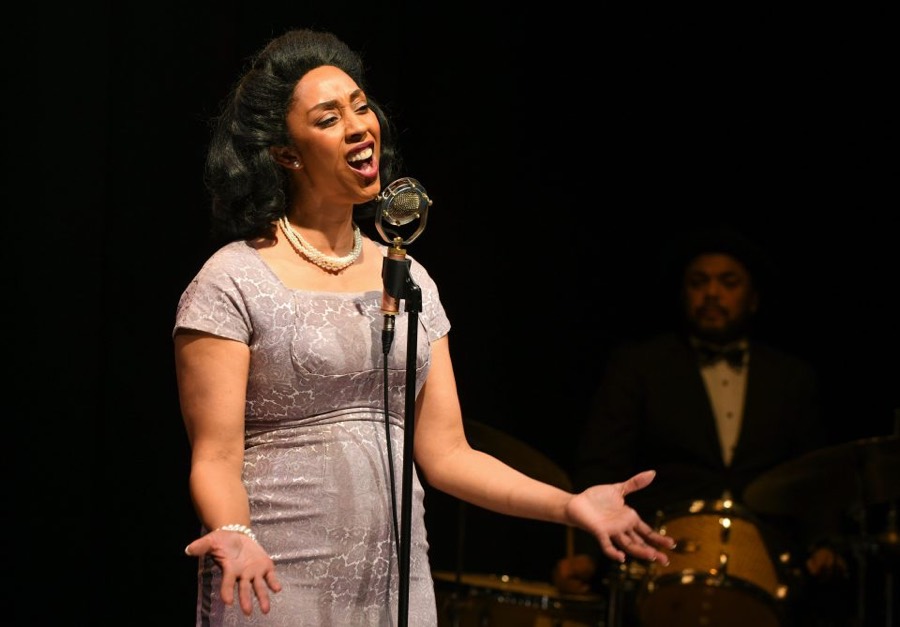 Woman with 1940s hairstyle and clothes singing at a vintage microphone.