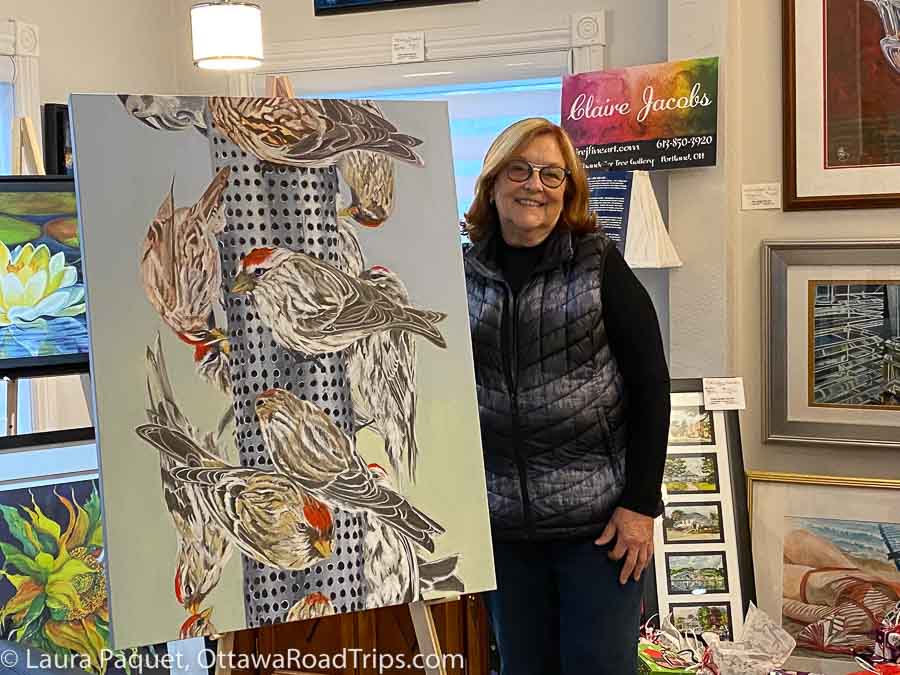 woman standing next to large painting of birds at a feeder
