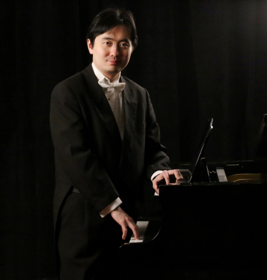 man in white tie and tails standing next to black piano, with one hand on the keyboard