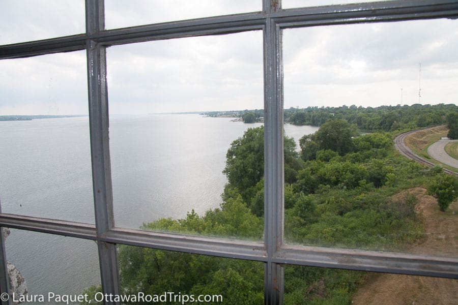 view of river, green trees and a railway track through old mullioned window at the battle of the windmill national historic site in prescott, ontario.