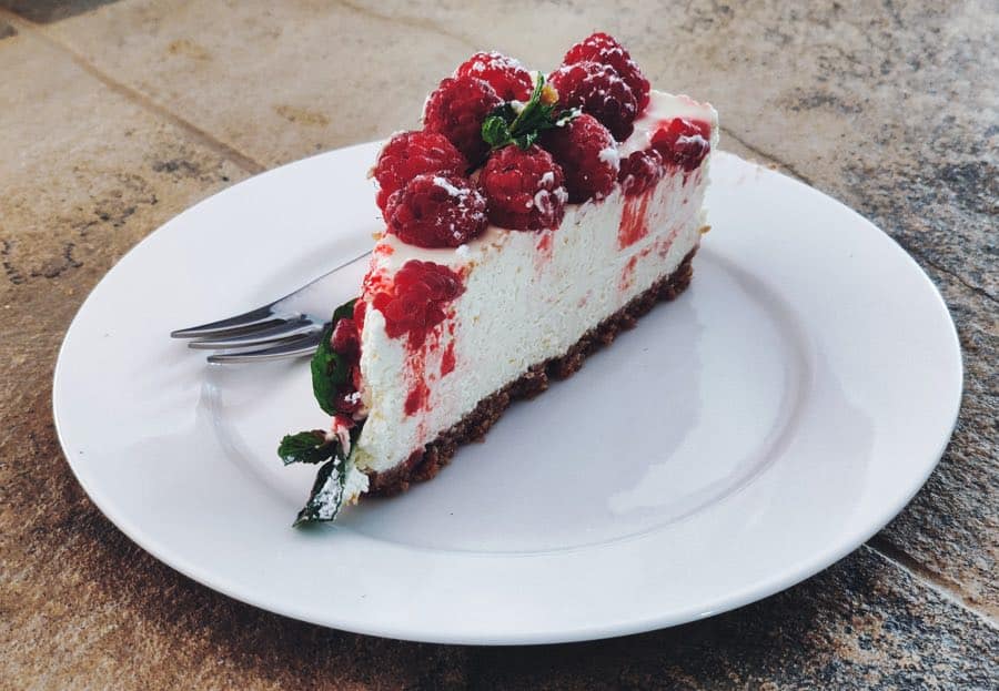 A wedge of raspberry cheesecake on a white plate.