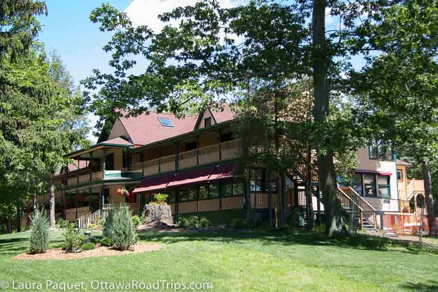 three-story wooden lakeside resort with wraparound porches with cream-coloured railings, green trim and red awnings.