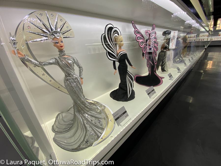 long display case of barbies wearing elaborate silver, black, white and pink bob mackie gowns