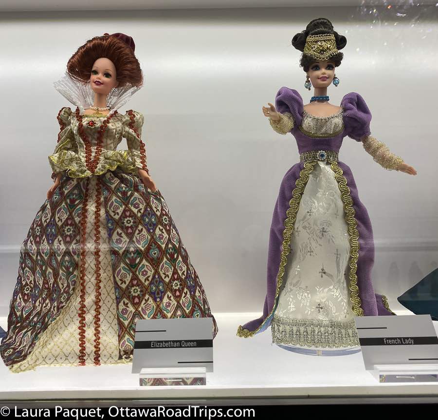 doll in multicoloured elizabethan gown and another barbie in a purple-and-gold historical dress