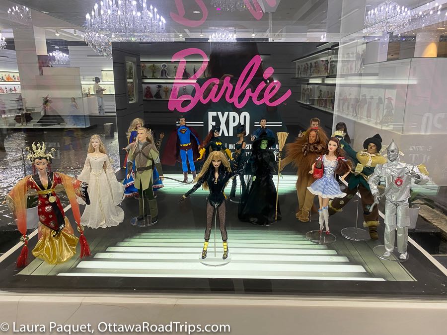 large glass display case with 16 barbies representing various tv and movie characters.