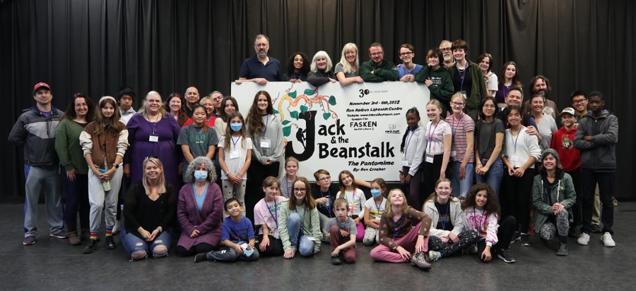 Large group of adults and kids standing and sitting around a large banner reading Jack in the Beanstalk.