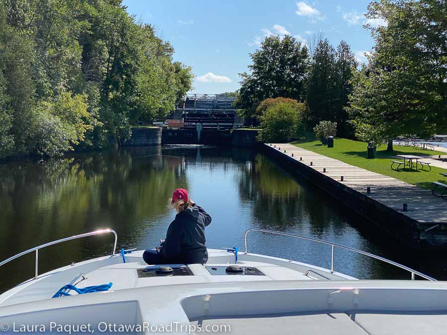 woman in red cap sitting on deck of le boat as it approaches long island lockstation on the rideau canal.