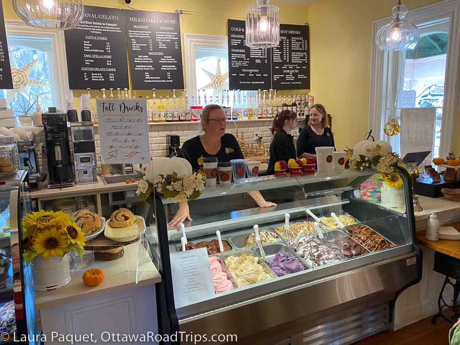 Three women behind display cases of gelato and cakes.