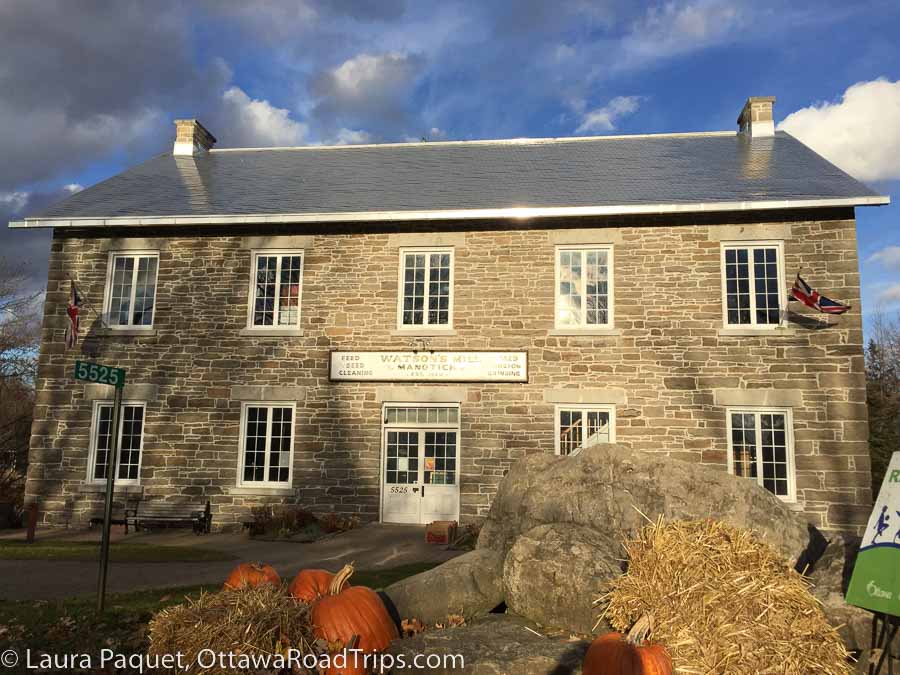 Watson's Mill in Manotick, a large limestone building with mullioned windows, with hay and pumpkins out front