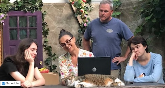 Woman, man and two teenagers sitting at a patio table looking at an open laptop.