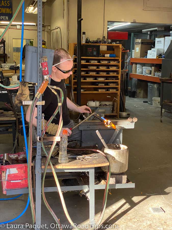 Man using a blow torch on a small glass vase in a glassblowing workshop.