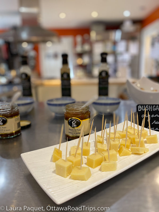 Cubes of cheese with tootpicks on a white tray with jars of chutney and bottles of dressing in the background.