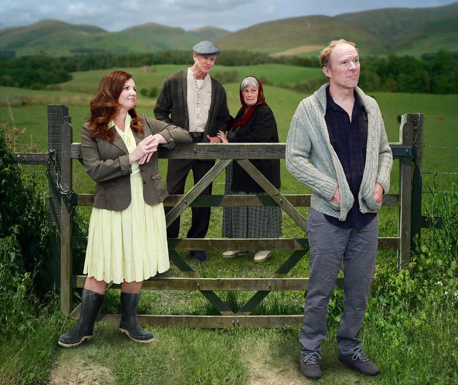 Two women and two men standing near a fence surrounded by green fields.