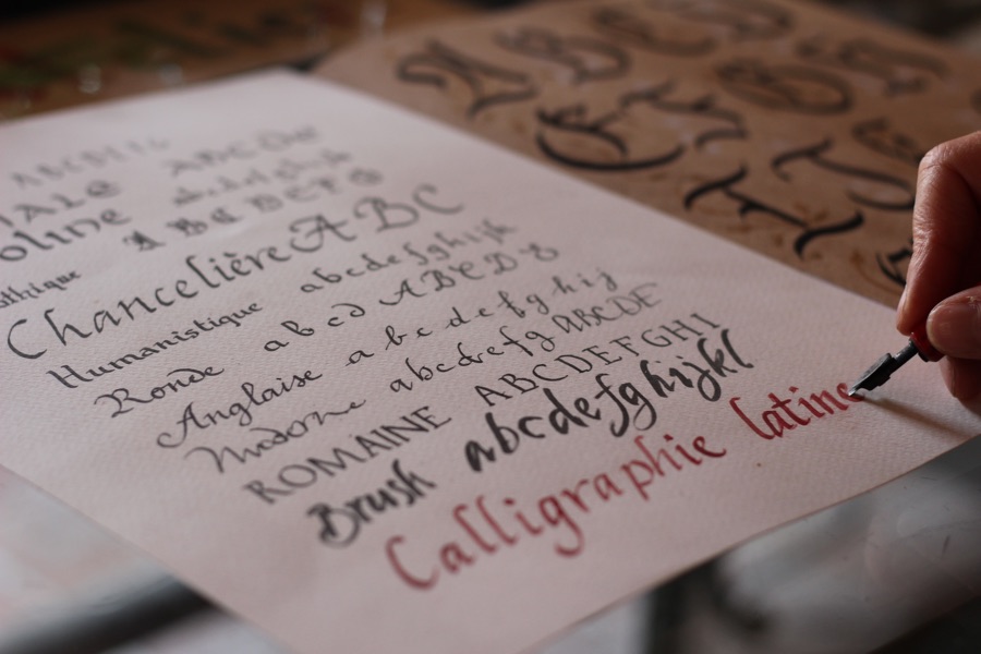 closeup of hand with calligraphy pen writing different fancy fonts on a white piece of paper