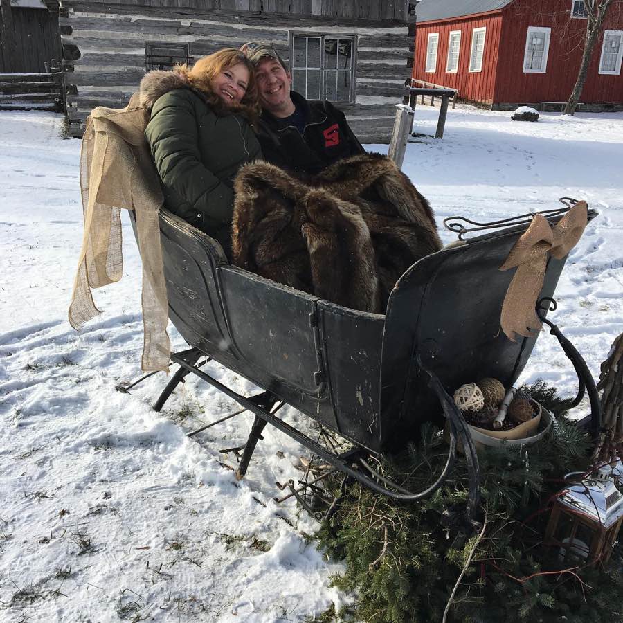 Woman and man in winter coats in a wooden sleigh decorated with gold ribbon.