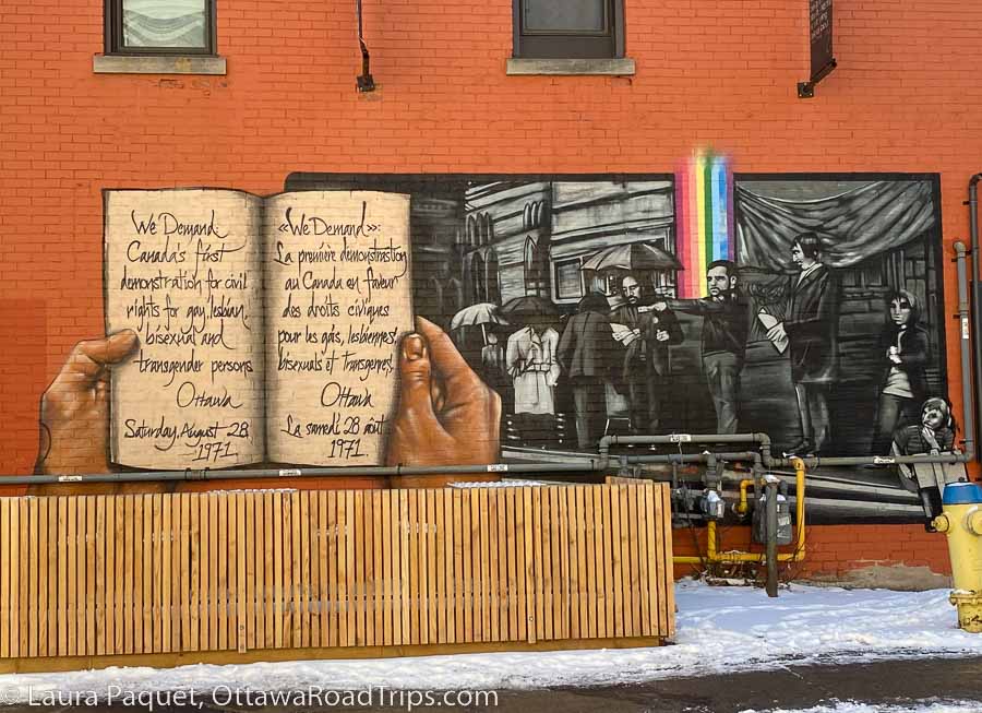 black-and-white mural (with rainbow) of lgbtq rights protesters in 1971, on a red brick wall in centretown.