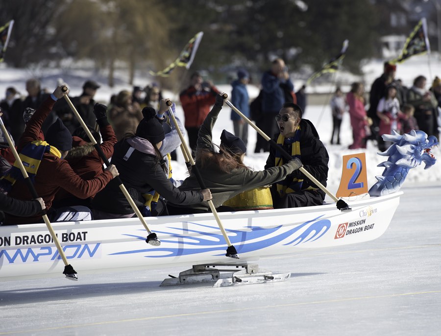 women using poles to propel a dragon boat across the frozen rideau canal, with spectators in background.