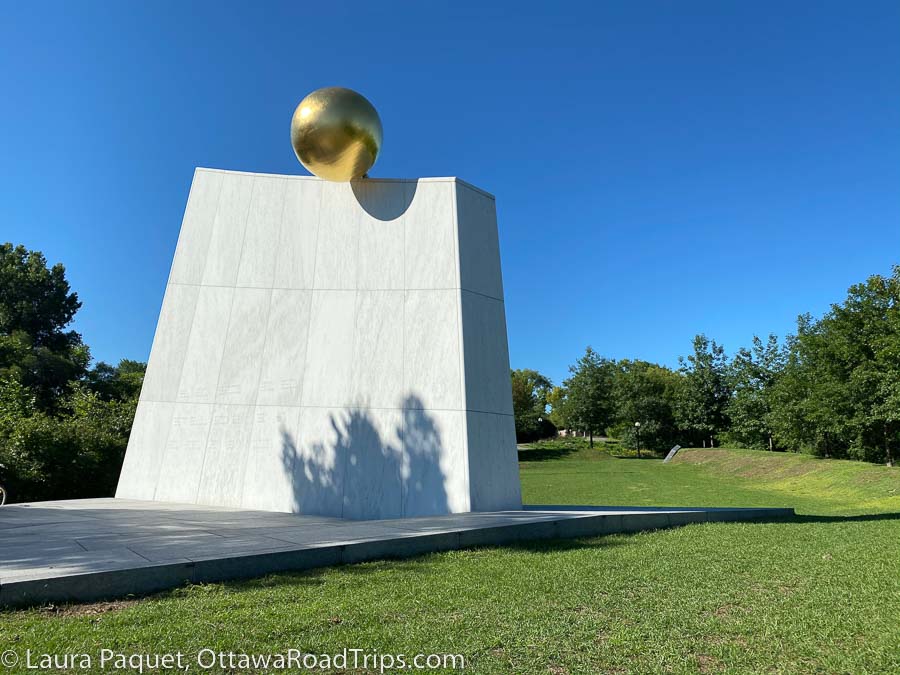 the royal canadian navy monument is a large white abstract monument with a gold sphere on top, surrounded by green lawns.