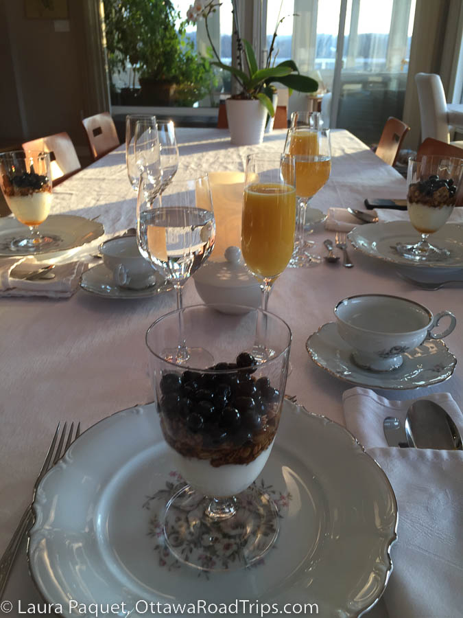 breakfast table set with white linen, glasses of orange juice and dishes of berries and yogurt