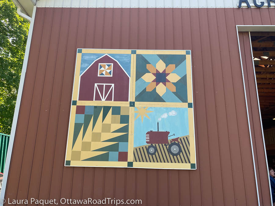 barn quilt depicting a barn, a flower, wheat and a tractor