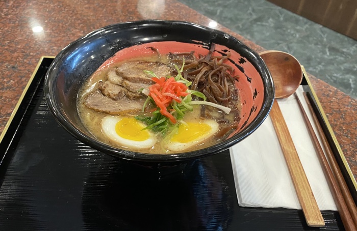 ramen with meat and eggs in a black and red bowl