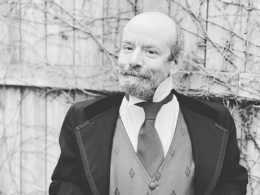 Black-and-white photo of man with beard in Victorian-style suit.