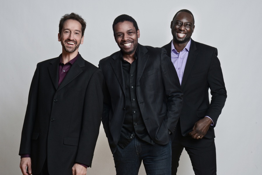 Three men in dark suits laughing and looking directly at the camera