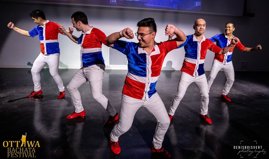 Five men in red, white and blue shirts, white pants and red shoes dancing in a triangular formation, facing the camera