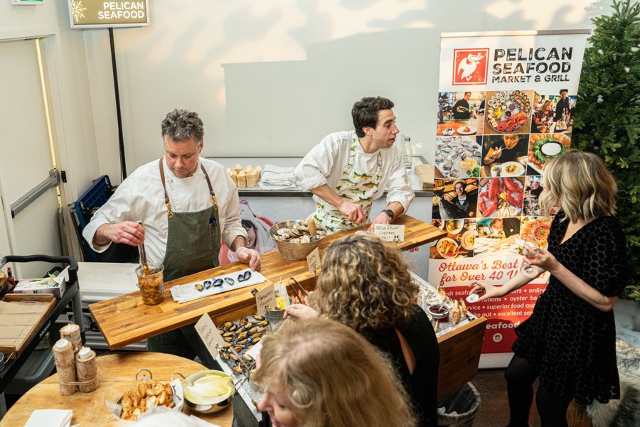 Two men in chef's aprons serving seafood to guests at an event booth.