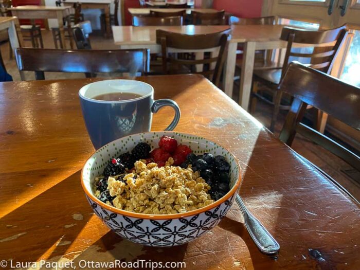 large bowl of yogurt, granola, blackberries, raspberries and blueberries on a wooden table, with a blue mug of tea behind