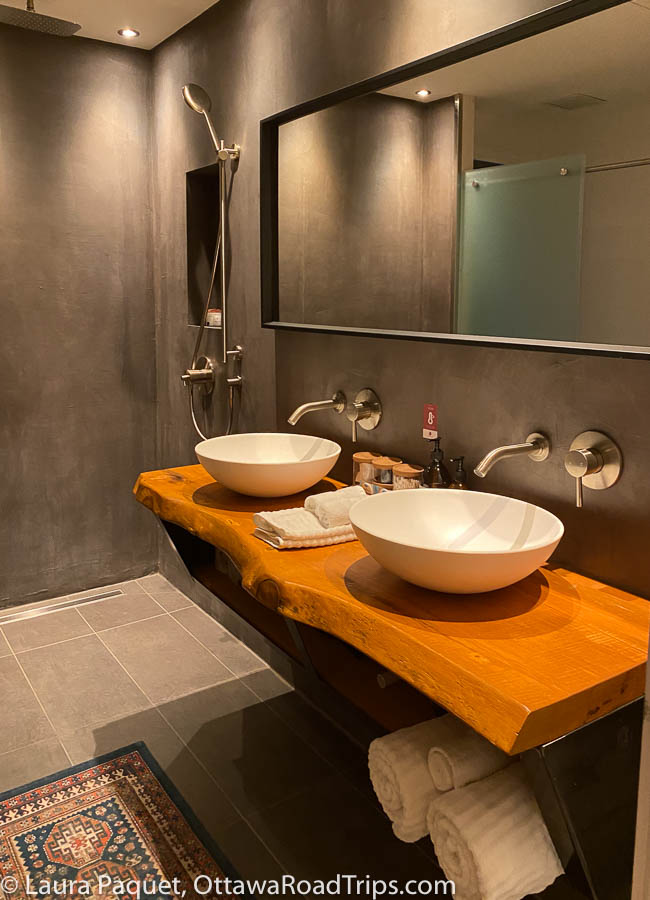 bathroom with dual vessel sinks, wood vanity, grey walls, and a rainfall shower head