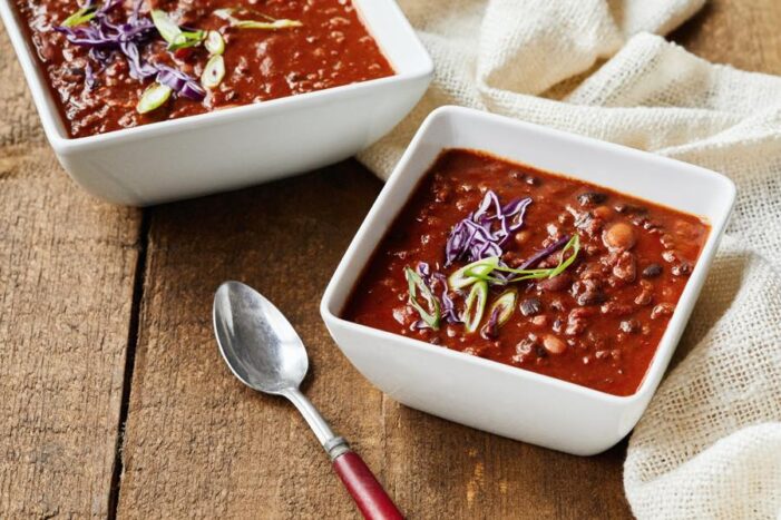 two square white bowls of chili on a wooden table