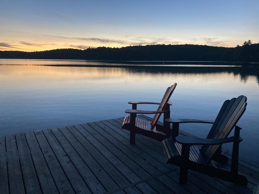 two muskoka chairs on a cottage dock at sunset