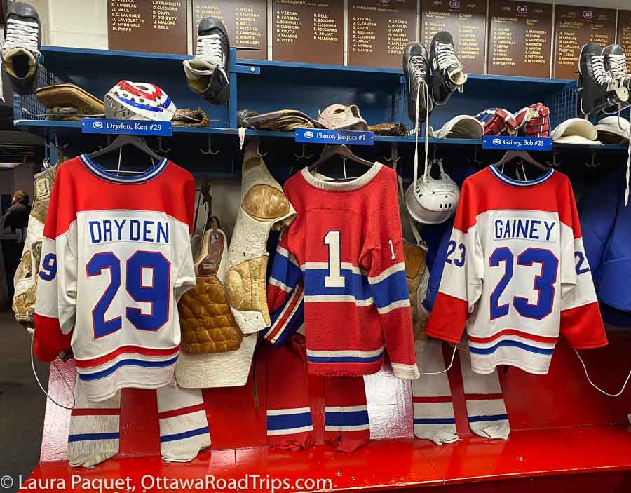 three red white and blue hockey jerseys (dryden, plante and gainey) in a reconstruction of the montreal canadiens dressing room.
