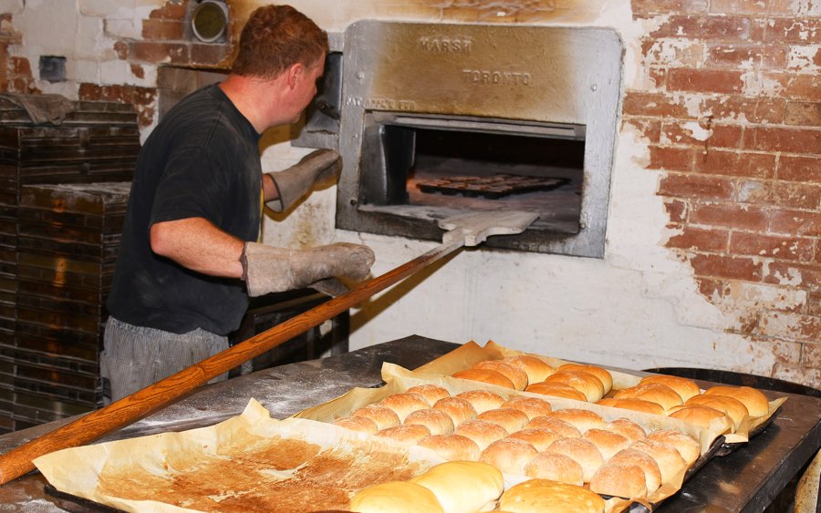 Man putting tray into wood-burning oven at Grahame's Bakery in Kemptville, Ontario.