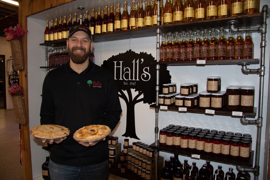 Man holding two pies in front of a display of apple ciders and jams at Hall's Apple Market in Brockville, Ontario.