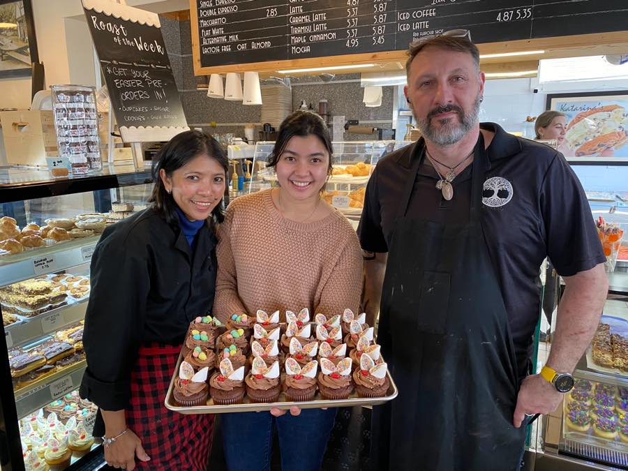 Three people standing with a tray of decorating cupcakes in front of display counters at Katarina's in Prescott, Ontario.