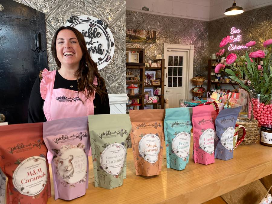 woman in pink apron behind wooden counter lined with colourful packages of caramels