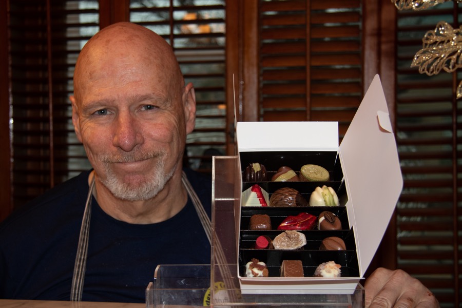 smiling man next to an open white box of colourful chocolates