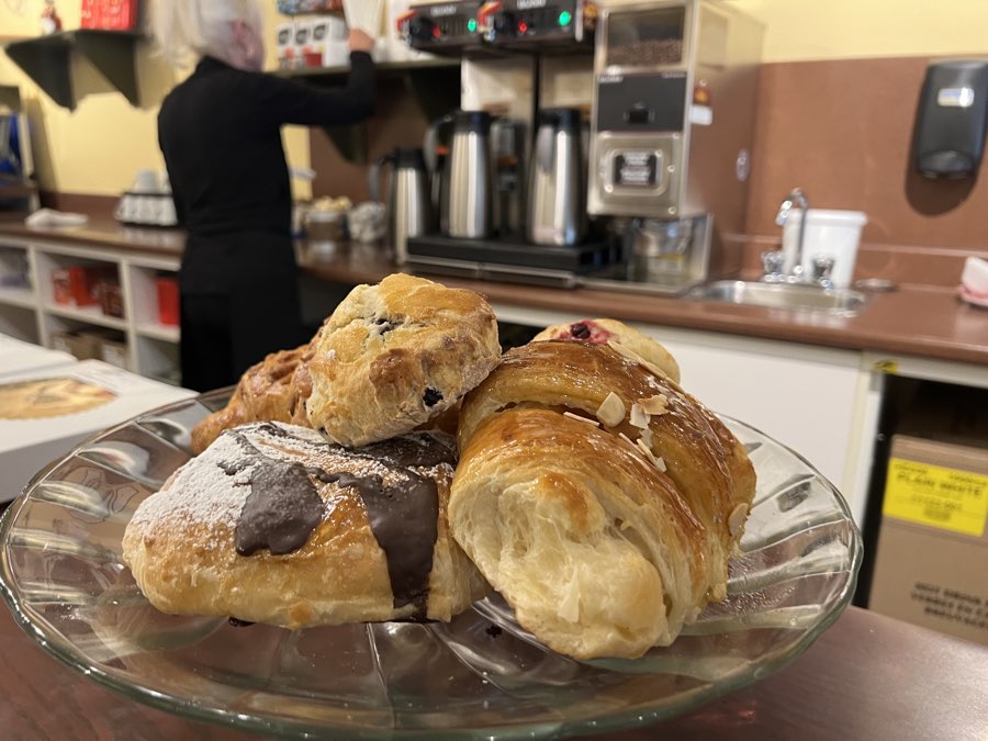 croissant, scone and other pastries on a glass plate on a cafe counter, with someone making coffee in background, at tait's Fresh Start in Brockville, Ontario.