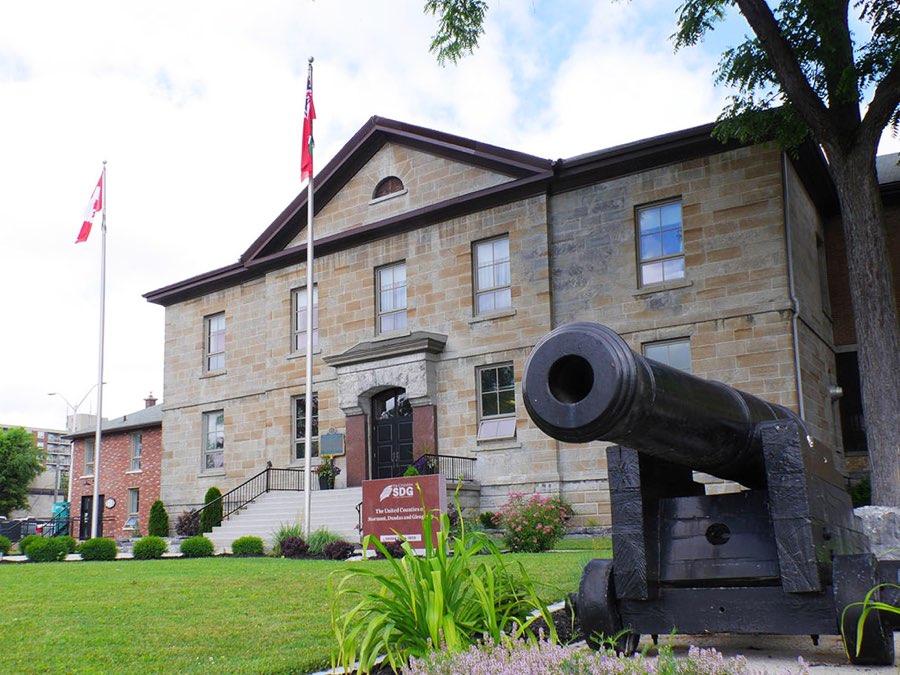 large stone georgian-style building with flags and a cannon out front. historic sdj jail in cornwall, ontario.