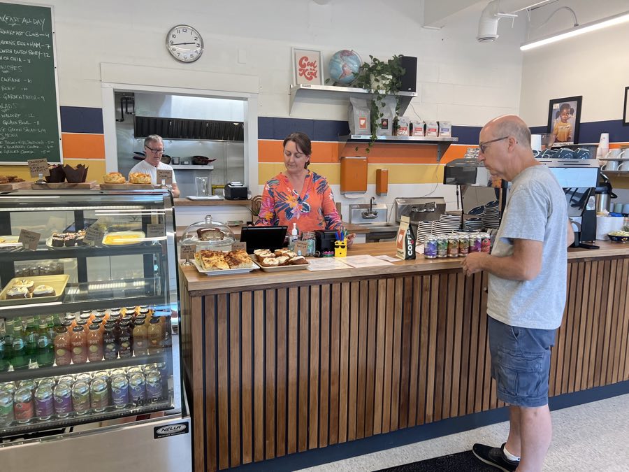 male customer at wooden counter with two staff members behind and baked goods on counter