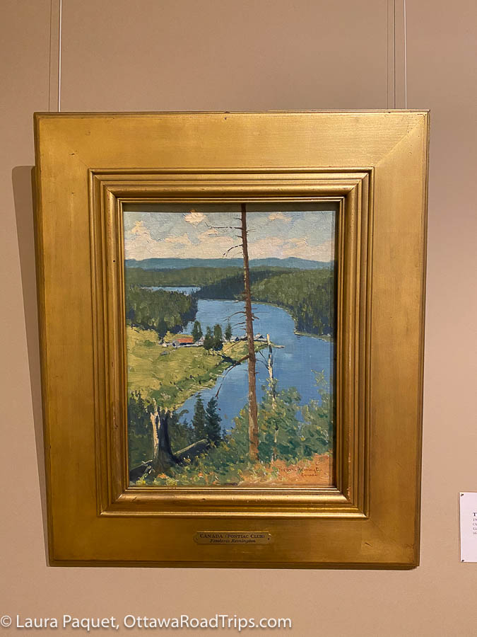 a painting of a river with wooded hills in the background, in a gilded frame, at the frederick remington art museum in ogdensburg, new york.