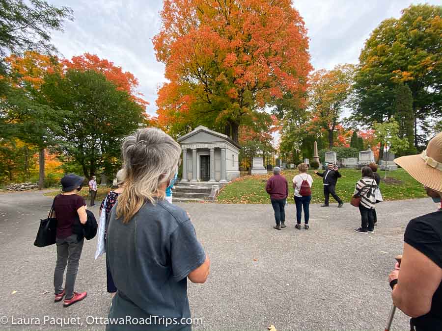 bright orange trees among green trees and headstones are an example of fall colours in ontario at beechwood cemetery.