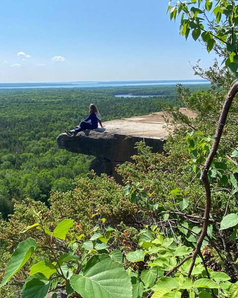 woman sitting on a flat stone outcrop looking over forests and a river on the cup and saucer trail.