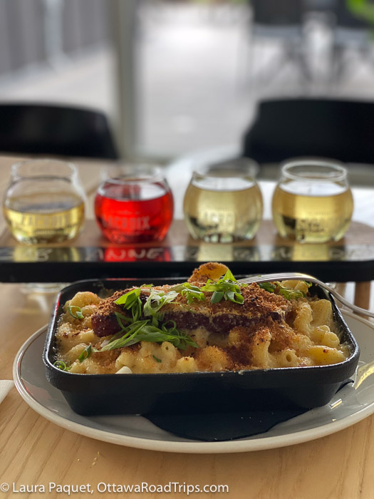 a black dish of macaroni and cheese, with flight of ciders in background