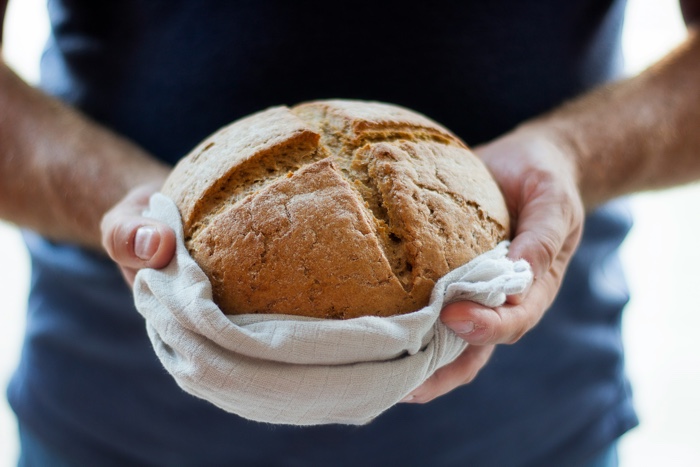 hands holding a round loaf of bread wrapped in a towel